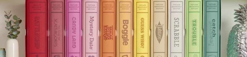 Colorful board game boxes arranged in a row with a pineapple on a white surface.